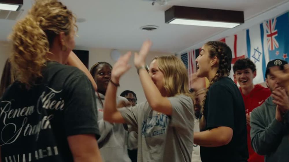 MACC 2026 campers high-fiving in a room lined with international flags